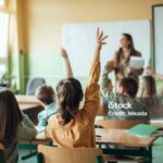 Students raising hands while teacher asking them questions in classroom