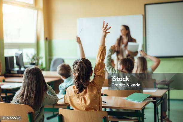 Students raising hands while teacher asking them questions in classroom
